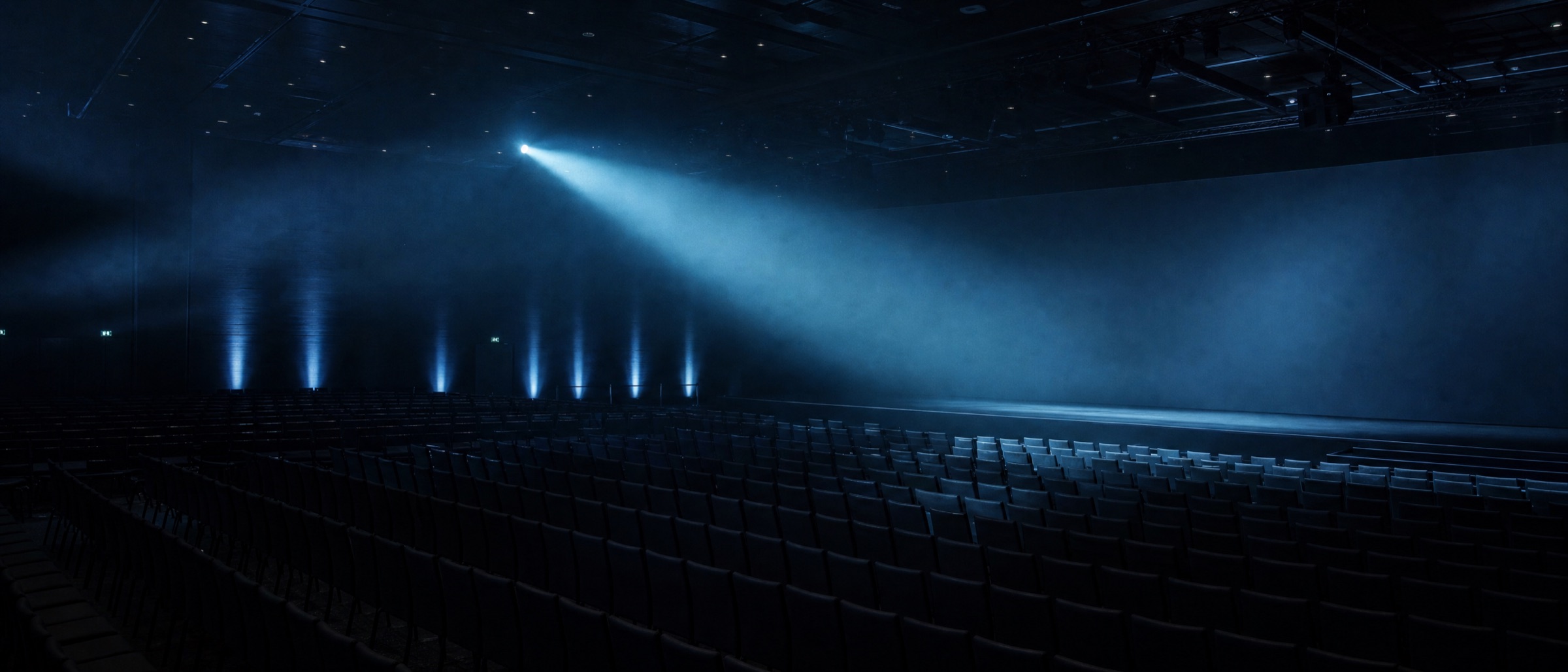 An empty enterprise keynote hall before doors open, lit by a single beam of light